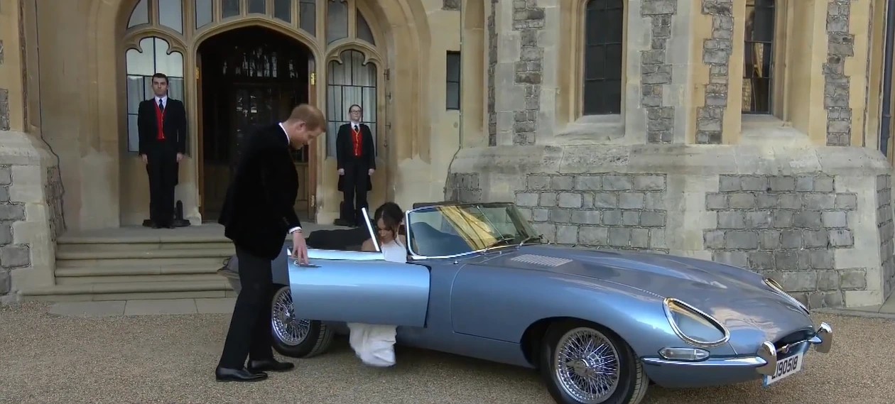 Harry is in black tie. They walk out to a silver-blue 1968 Jaguar E-Type convertible with the top down