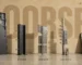 Five steel doorset components standing in a row against a wall painted with the word DOORSET, from cutaway leaf through to certificate