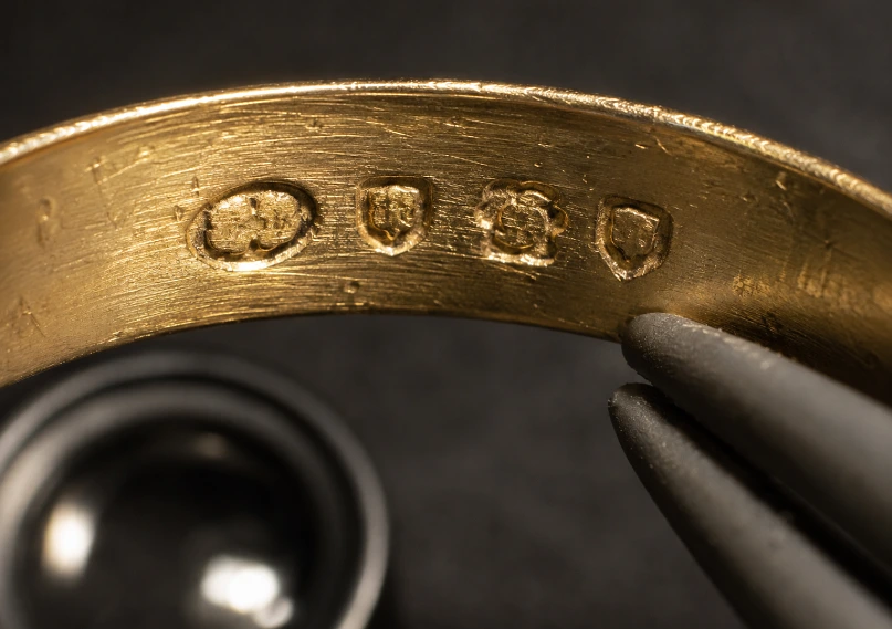 Macro view of four small punched hallmarks struck inside a worn gold ring shank held in tweezers
