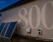 Two solar panels on a freestanding frame plugged into an outdoor socket, against a wall painted with a large numeral 800