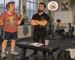 Cartoon of a man holding a banana asking a trainer a question beside a squat rack in a small gym